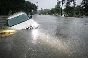 An SUV is stranded in a ditch along a stretch of street flooding during a severe storm Thursday in Spring, Texas.