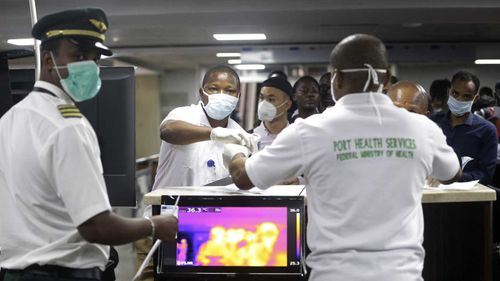 A Nigerian port health official, right, uses a thermometer to screen Ethiopian Airline cabin crews for COVID-19 virus.