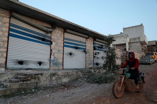 A Syrian man rides his scooter as he passes next to a shops after an operation by the U.S. military in the Syrian village of Atmeh, in Idlib province, Syria, Thursday, Feb. 3, 2022.
