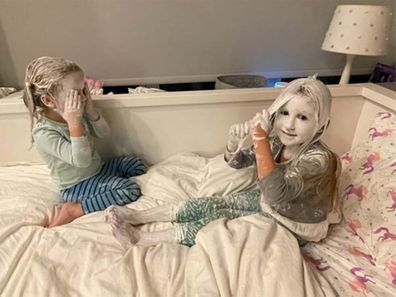 Two little girls sitting in bed covered head to toe in white diaper cream
