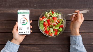 Woman counting calories on app and eating a salad