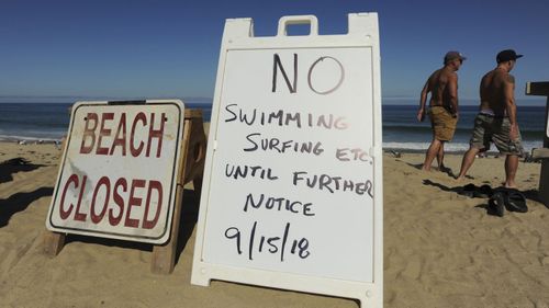 Flowers were placed at the base of a sign that said "No swimming surfing etc. until further notice," but some people were paddle boarding in the water