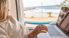 View of a woman working on her laptop from a wild camping spot, Sardinia, Italy. Digital nomad lifestyle