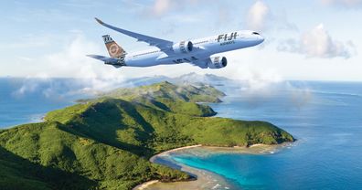 A Fiji Airways plane flying over an island and blue sea.