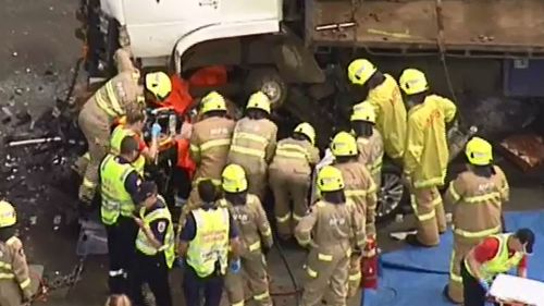 Emergency crews prepare to lift the second truck off the crushed vehicle. (9NEWS)