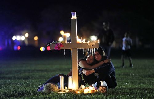 People comfort each other as they sit and mourn at one of seventeen crosses, Feb. 15, 2018, after a candlelight vigil for the victims of the shooting at Marjory Stoneman Douglas High School, in Parkland, Florida.