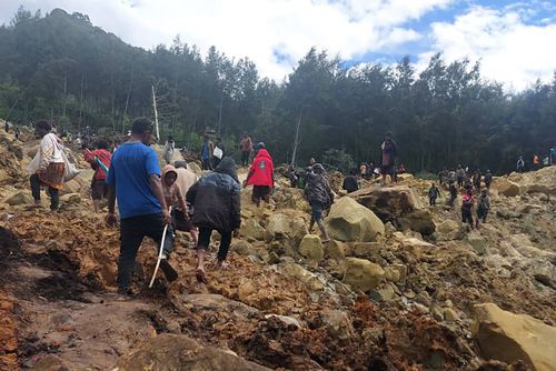 In this photo provided by the International Organization for Migration, people cross over the landslide area to get to the other side in Yambali village.