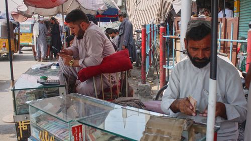 A man at a street stand for money exchange checks his cellphone after some networks were restored following an outage that began Monday in Jalalabad, Afghanistan.
