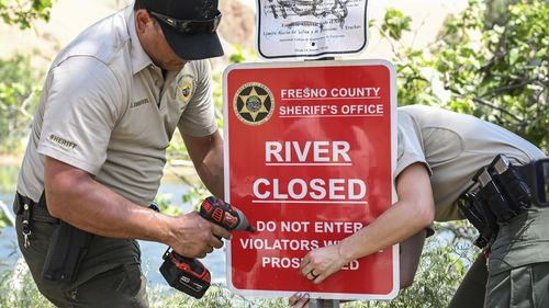 Fresno County Sheriff's Office reservists attach a sign to a post to alert people that the the Kings River is closed due to dangerously high water levels, on Monday, May 22, 2023, near Sanger, Calif. The body of a 4-year-old boy was recovered Monday from the surging California river that is closed to recreational use, a day after his 8-year-old sister died when the siblings were swept away by the current, authorities said. (Craig Kohlruss/The Fresno Bee via AP)