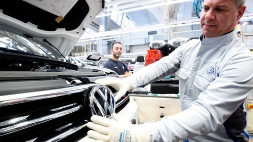An employee shows a VW logo shortly before installation in a Volkswagen Touran in final assembly at the VW plant.
