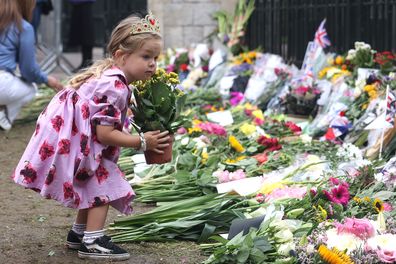 A child wearing a crown places a pot of flowers with other tributes at The Long Walk gates in front of Windsor Castle.