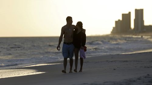 In this March 12, 2020 photo, people walk on the beach in Gulf Shores, Ala. The spring of coronavirus feels a lot like the summer of oil to residents along the Gulf Coast. Bars and restaurants are empty in Florida because of an invisible threat nearly a decade after the BP oil spill ravaged the region from the ocean floor up.