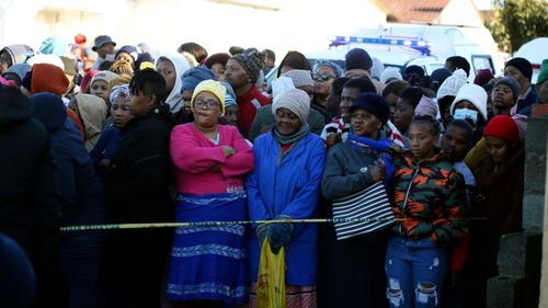 People stand behind a police cordon outside a nightclub in East London, South Africa, Sunday June 26, 2022. South African police are investigating the deaths of at least 20 people at a nightclub in the coastal town of East London early Sunday morning. It is unclear what led to the deaths of the young people, who were reportedly attending a party to celebrate the end of winter school exams. 