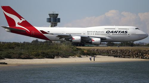 Two people watch from a beach as a Qantas plane taxies on the runway at Sydney Airport.