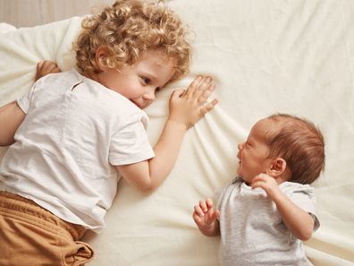 Toddler and baby sibling laying on a bed