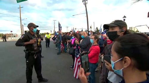 Law enforcement officials stand at a perimeter as Trump supporters gather to wish the President well as he left the hospital today.