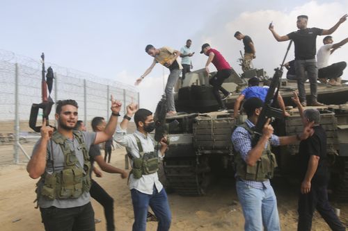 Palestinian militants celebrate by an Israeli tank at the border fence of the Gaza Strip on Saturday, Oct. 7, 2023.  