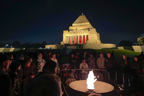 People gather around the flame during the ANZAC Day dawn service at the Shrine of Remembrance in Melbourne on April 25, 2022. 
