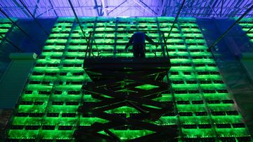 A technician on a cherry picker inspects racks of illuminated mining rigs at the Minto cryptocurrency mining center in Nadvoitsy, Russia. Bitcoin has dropped precipitously in recent days.