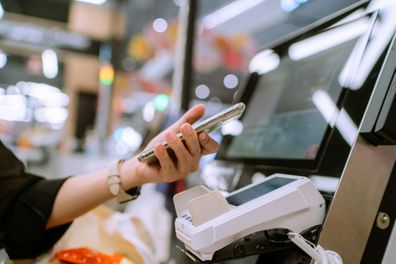 Asian woman using her mobile phone making contactless payment in supermarket.