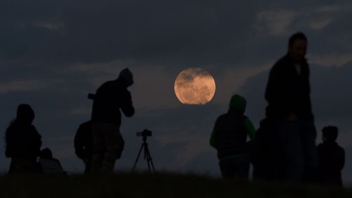 A crowd watches as the full moon is seen between the clouds from Bald Hill, south of Sydney. (AAP)
