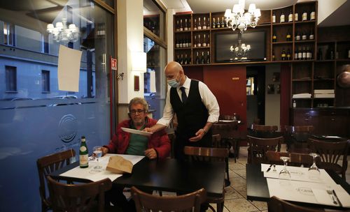 In this photo taken on Tuesday, May 19, 2020, a waiter tends to a customer at the "La Rotonda di Segrino" restaurant in Milan, Italy.