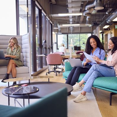 Businesswomen Having Informal Meeting In Breakout Seating Area Of Modern Open plan Office