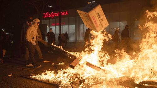 In this May 29, 2020, photo, a protester pulls a burning board from a fire set in response to the death of George Floyd in downtown Oakland, California