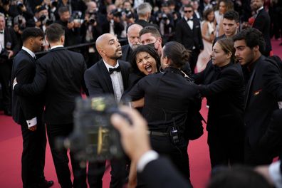 A protestor wearing body paint that reads "Stop Raping Us" in the color of the Ukrainian is removed from the red carpet at the premiere of the film 'Three Thousand Years of Longing' at the 75th international film festival, Cannes, southern France, Friday, May 20, 2022. 