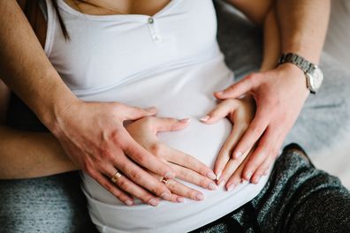 Cropped image of husband holding belly of his pregnant wife making symbol heart hands. 