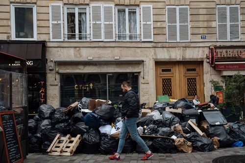 A man walks past uncollected garbage in Paris, Monday, March 13, 2023.