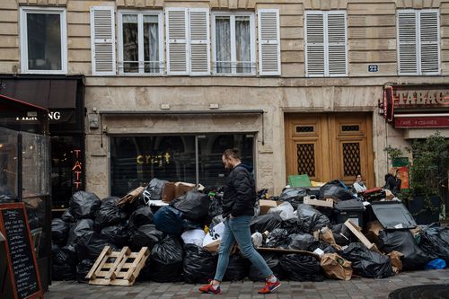 A man walks past uncollected garbage in Paris, Monday, March 13, 2023.