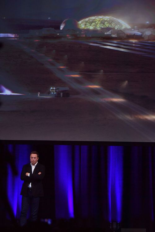 CEO of Tesla and Director of SPACEX, Elon Musk is seen delivering a presentation, with a representation of what he imagines a human colony on mars to look like on the screen behind him