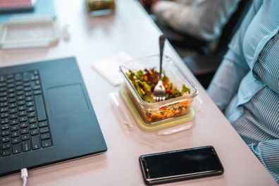 High angle view of a female office employee eating lunch in front of a computer. 