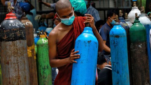     In this archive image on July 28, 2021, a Buddhist monk wearing a face mask holds an oxygen tank for refilling outside the Naing Oxygen Factory in the South Dagon Industrial Zone in Yangon, Myanmar. 