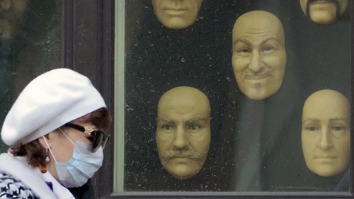 A woman wearing a face mask to protect against coronavirus walks past wax faces displayed in a window of a wax museum in St.Petersburg, Russia, Monday, May 4, 2020. (AP Photo/Dmitri Lovetsky)