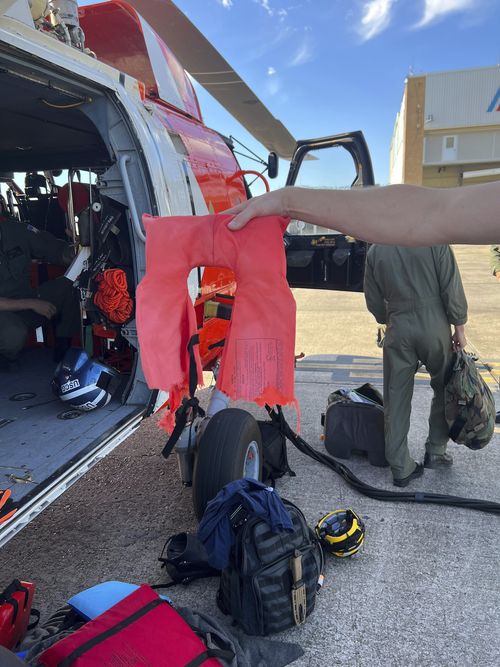 In this image provided by the U.S. Coast Guard, a Coast Guard Air Station New Orleans aircrew member holds up a torn life jacket from a recent rescue off the coast of Empire, La., on Oct. 9, 2022. Three men whose fishing boat sank in the Gulf of Mexico off the Louisiana coast were rescued after surviving for more than a day despite being attacked by sharks that inflicted deep cuts on their hands and shredded one of their life jackets, according to their rescuers. 