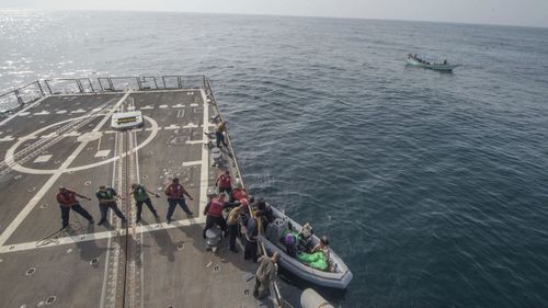 US Navy Sailors aboard the guided-missile destroyer USS Jason Dunham (DDG 109) heave a line to on load weapons seized from a skiff following a flag verification boarding as part of maritime security operations. (AP)