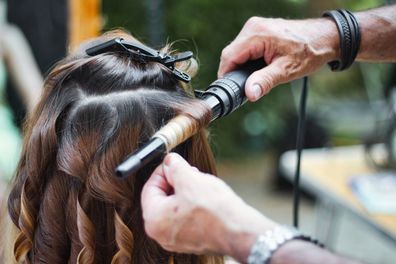 Back of the head of a young woman having her hair curled by a stylist using a curling iron