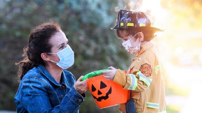 Woman with her son about to trick-or-treat while wearing face masks