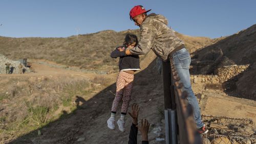 A migrant from Honduras pass a child to her father after he jumped the border fence to get into the U.S. side to San Diego, Calif., from Tijuana, Mexico.