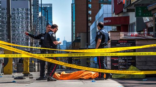 Police officers stand by a body covered on the sidewalk in Toronto.