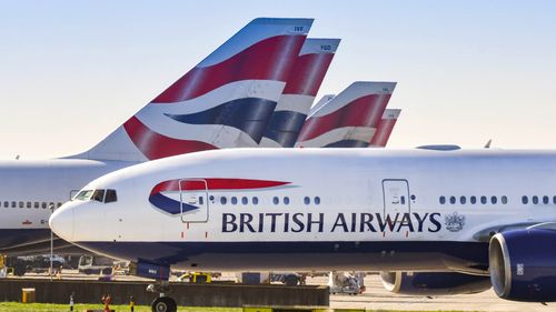 Boeing 777 long haul airliner operated by British Airways taxiing for take off at London Heathrow Airport past tail fins of the company's other aircraft.