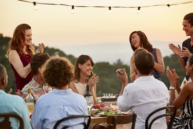 Happy male and female friends clapping while enjoying dinner party
