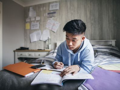 Teenage boy lying on his bed while concentrating on homework for his exams.