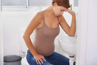 A pregnant woman struggling with morning sickness in the bathroom