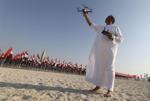 Un bărbat se pregătește să arboreze o dronă deasupra steagurilor naționale ale Emiratelor Arabe Unite pentru a sărbători Ziua Drapelului în Dubai, Emiratele Arabe Unite.