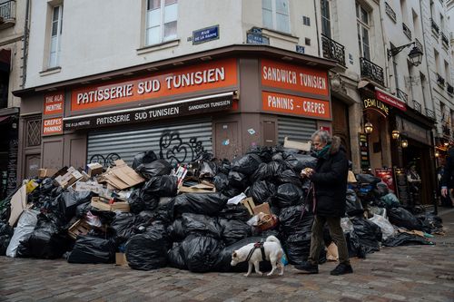 A man walks past piles of garbage in Paris. A contentious bill that would raise the retirement age in France from 62 to 64 got a push forward with the Senate's adoption of the measure amid strikes, protests and uncollected garbage piling higher by the day.