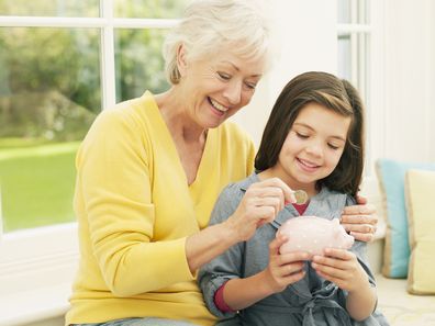 Grandmother putting coin into granddaughters piggy bank - stock photo