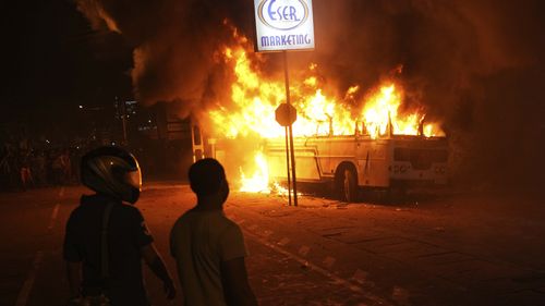 Sri Lankans watch after setting a bus on fire during a protest outside the President's private residence on the outskirts of Colombo. 